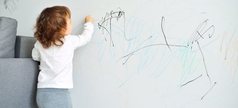 Little kid drawing with crayons on a wall.