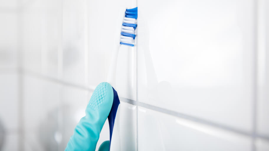 Cleaning grout with a toothbrush on a white tiled wall