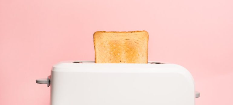 A white toaster with lightly toasted bread on pink backgroud