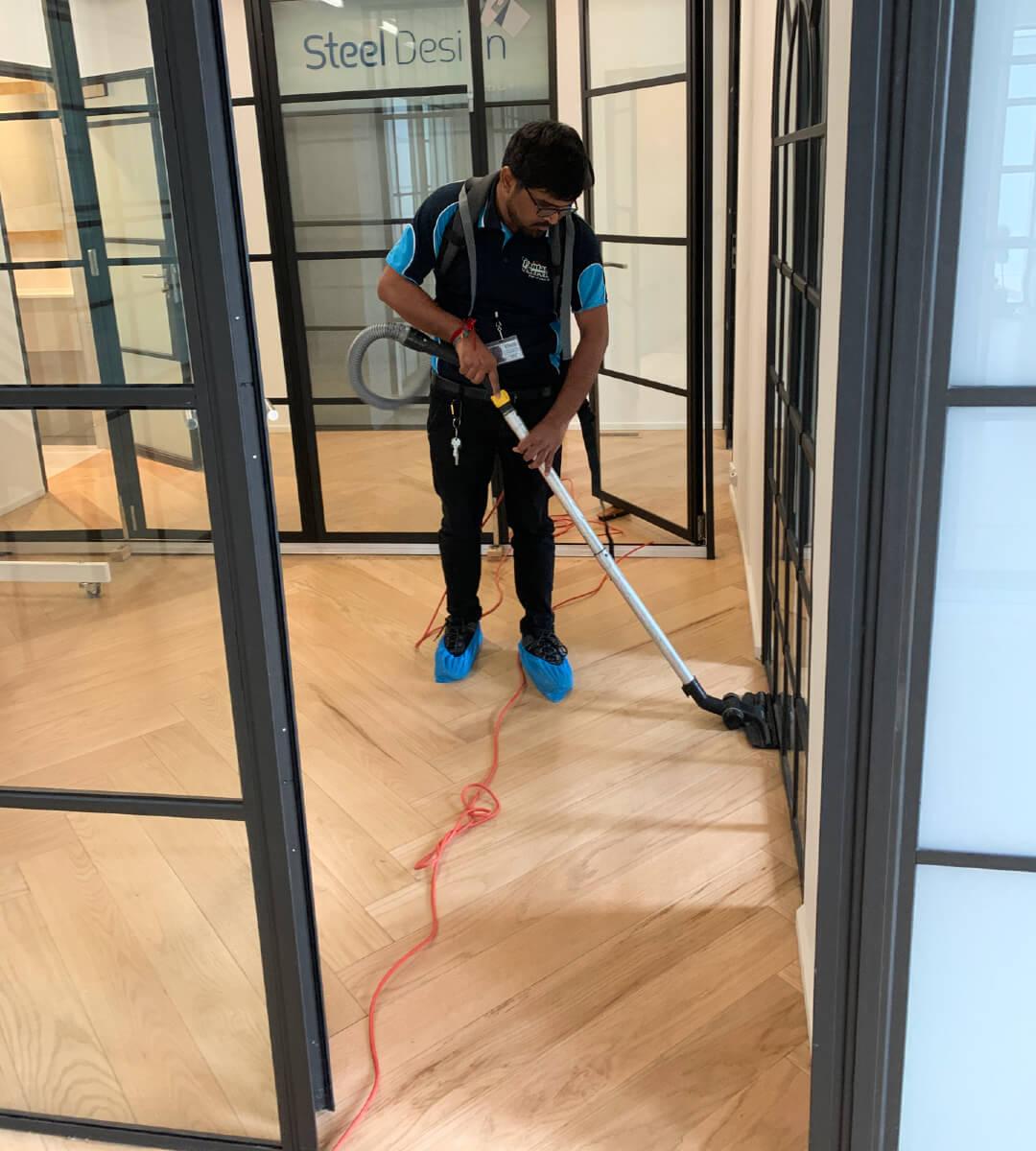 Commercial Cleaning services - Professional cleaner vaccuuming the wooden floor of an office